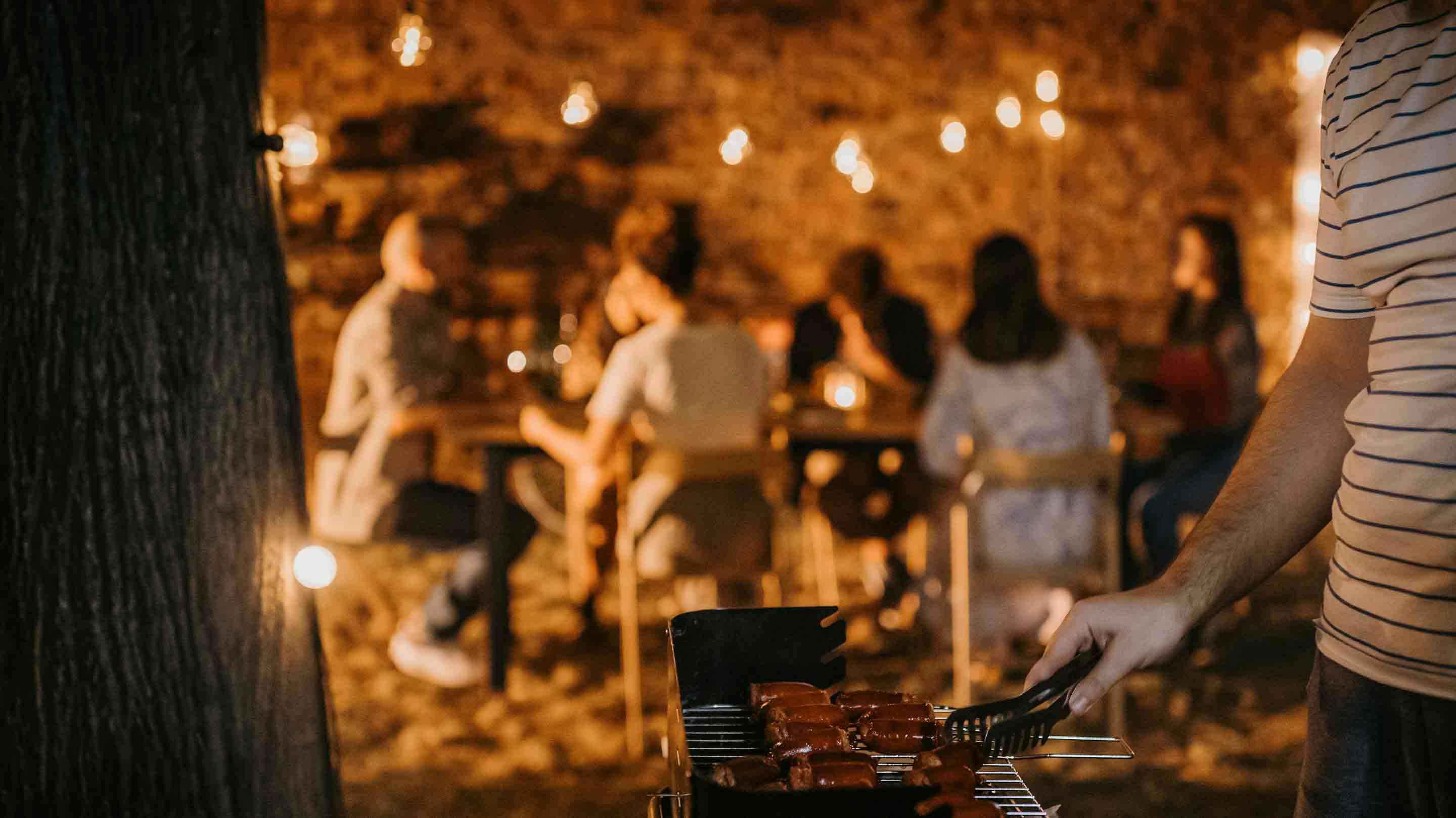 Przyjaciele cieszący się wieczorem przy grillu z bajkową dekoracją światła.